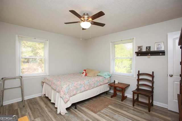 bedroom with multiple windows, a textured ceiling, baseboards, and wood finished floors