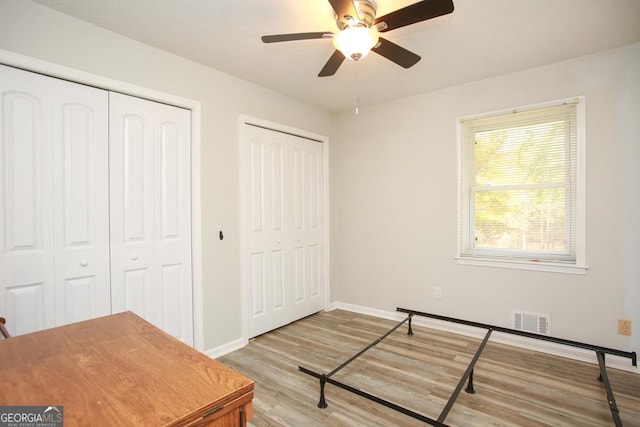 bedroom with visible vents, multiple closets, light wood finished floors, baseboards, and ceiling fan