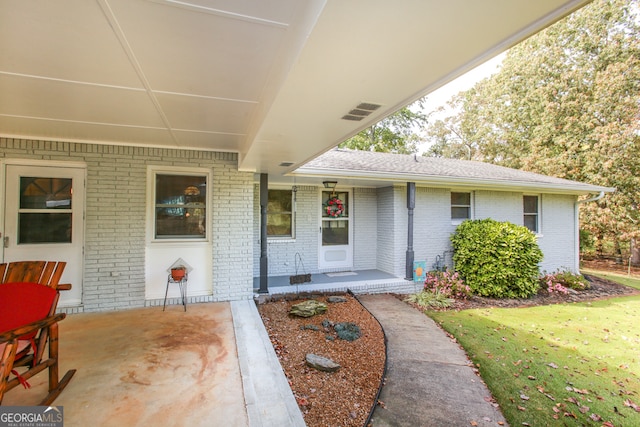 view of exterior entry with a patio and a lawn