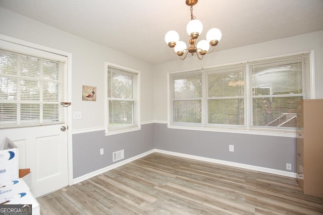 unfurnished dining area with a notable chandelier, visible vents, baseboards, and light wood-style floors