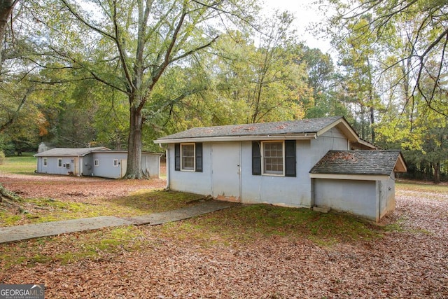 view of front facade with concrete block siding, a wooded view, and a shingled roof