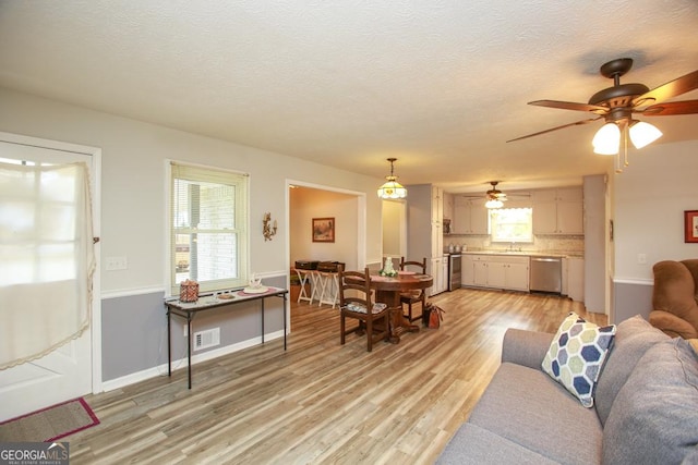 living room with baseboards, visible vents, a textured ceiling, and light wood-style floors