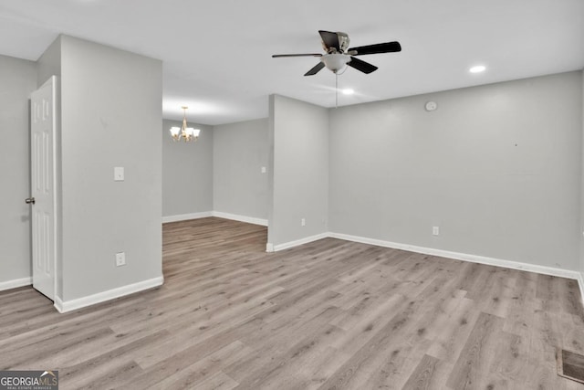 empty room featuring ceiling fan with notable chandelier and light hardwood / wood-style floors