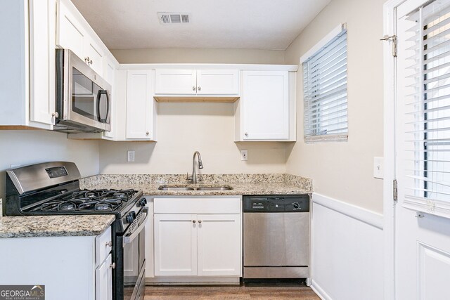 kitchen featuring stainless steel appliances, sink, light wood-type flooring, white cabinetry, and light stone counters