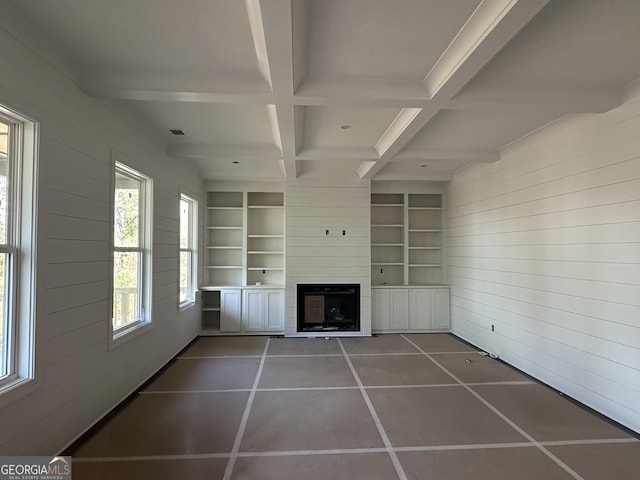 unfurnished living room featuring wooden walls, coffered ceiling, dark tile patterned flooring, built in shelves, and beamed ceiling