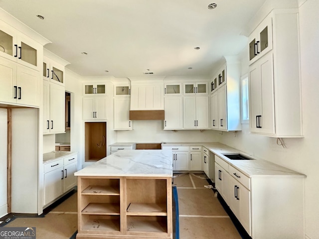 kitchen featuring sink, light stone countertops, white cabinets, and a kitchen island