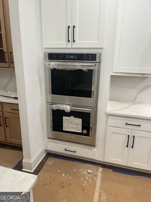 interior details with stainless steel double oven, light stone countertops, and white cabinets