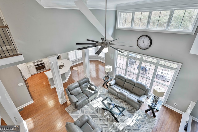 living room with a high ceiling, ceiling fan, light hardwood / wood-style floors, and crown molding