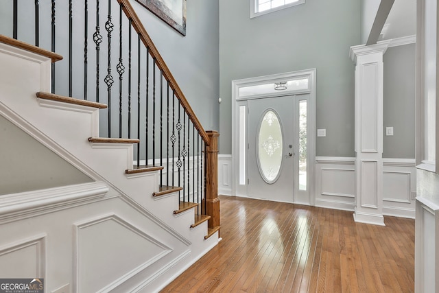 entryway featuring decorative columns, a towering ceiling, light hardwood / wood-style floors, and plenty of natural light