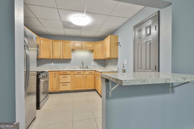 kitchen featuring a paneled ceiling, appliances with stainless steel finishes, light tile patterned floors, sink, and a breakfast bar area