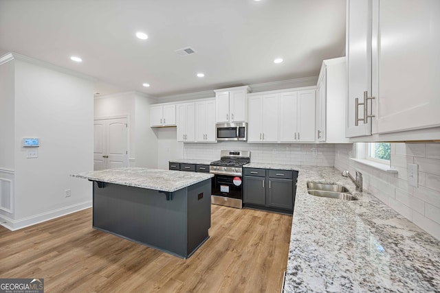 kitchen with a kitchen bar, stainless steel appliances, sink, light hardwood / wood-style flooring, and white cabinetry