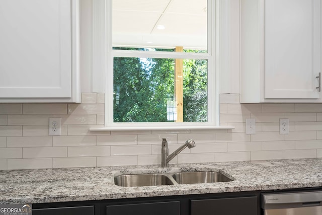 kitchen featuring decorative backsplash, light stone counters, stainless steel dishwasher, sink, and white cabinetry