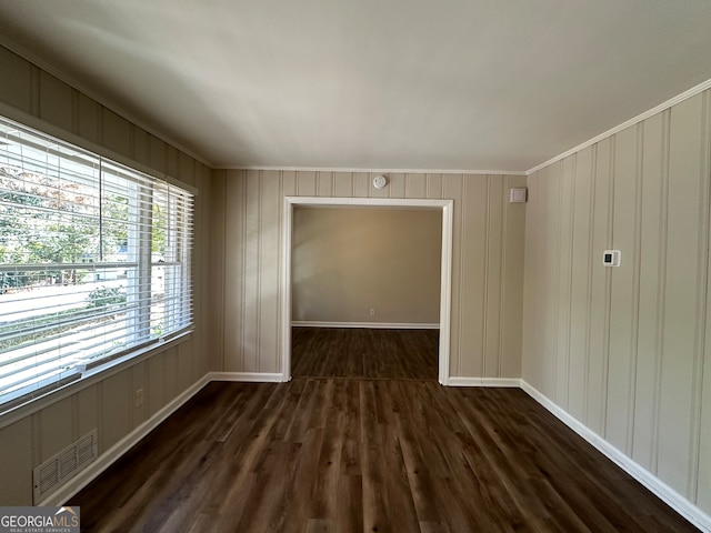 empty room with dark wood-type flooring, crown molding, and wood walls