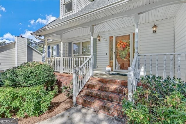 doorway to property featuring a porch and a shingled roof