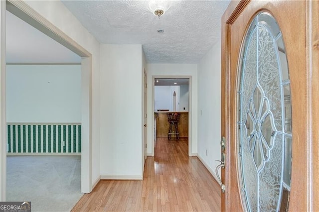 hallway featuring wood finished floors, baseboards, and a textured ceiling