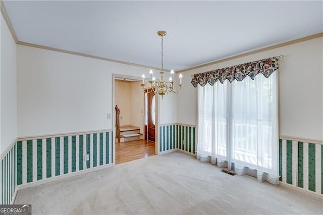 carpeted empty room featuring a chandelier, ornamental molding, and wainscoting