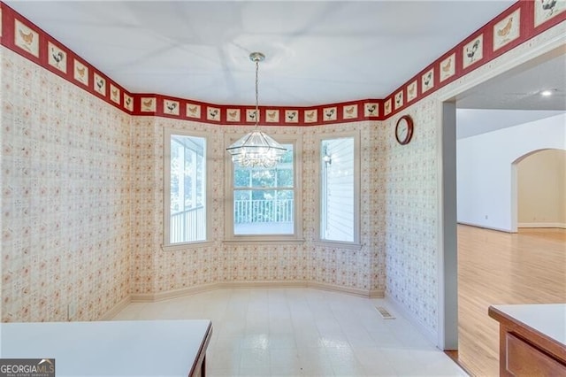 unfurnished dining area featuring wallpapered walls, a chandelier, baseboards, and arched walkways
