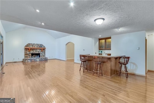 bar with light hardwood / wood-style floors, a stone fireplace, a textured ceiling, and lofted ceiling