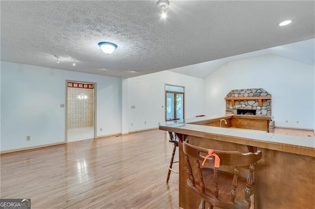 kitchen with tile countertops, baseboards, light wood-style flooring, vaulted ceiling, and a textured ceiling