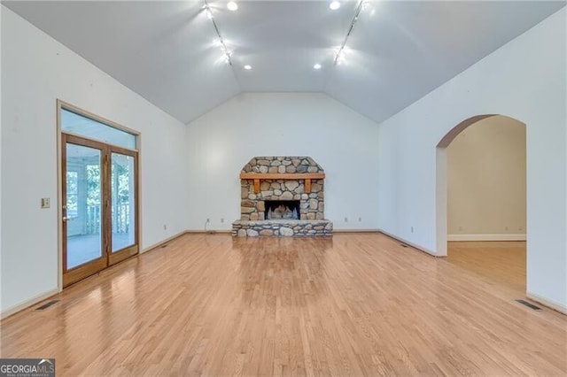 unfurnished living room with light hardwood / wood-style floors, a stone fireplace, vaulted ceiling, and track lighting