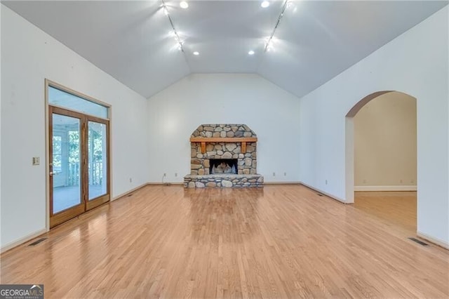 unfurnished living room with light wood finished floors, a stone fireplace, baseboards, arched walkways, and vaulted ceiling