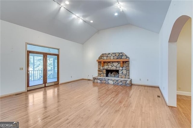 unfurnished living room with track lighting, light wood-style flooring, arched walkways, lofted ceiling, and baseboards