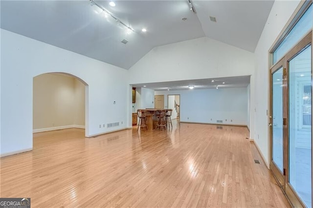 living room with rail lighting, light wood-style flooring, arched walkways, baseboards, and high vaulted ceiling