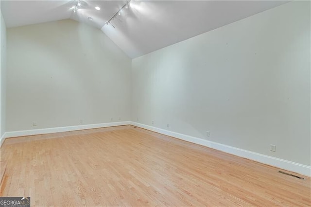unfurnished room with vaulted ceiling, light wood-style floors, baseboards, and rail lighting