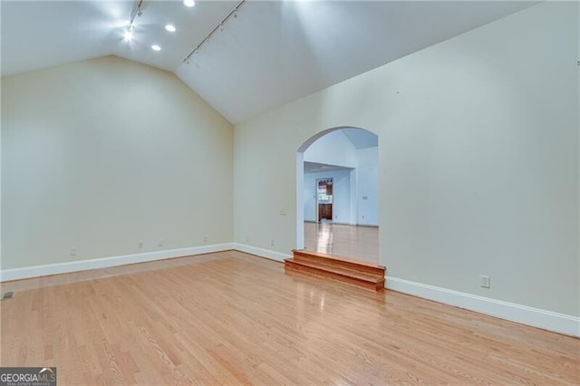 unfurnished living room featuring rail lighting, vaulted ceiling, and light wood-type flooring