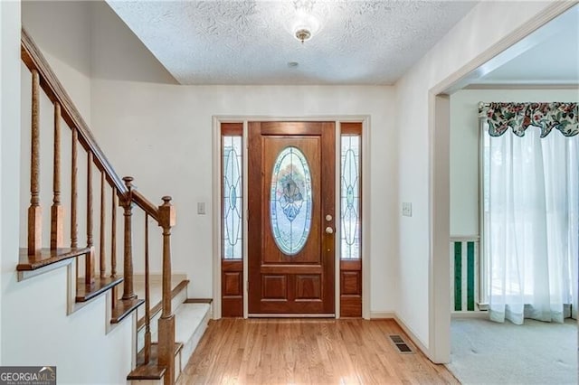 foyer with stairway, a textured ceiling, light wood-type flooring, and baseboards