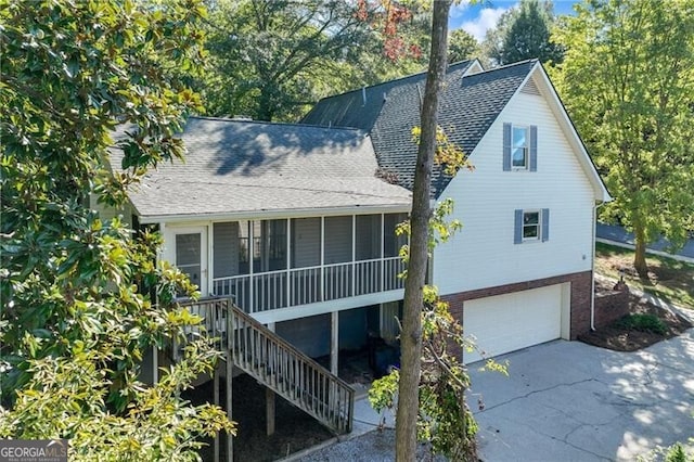 view of front of home with a shingled roof, an attached garage, stairway, concrete driveway, and a sunroom