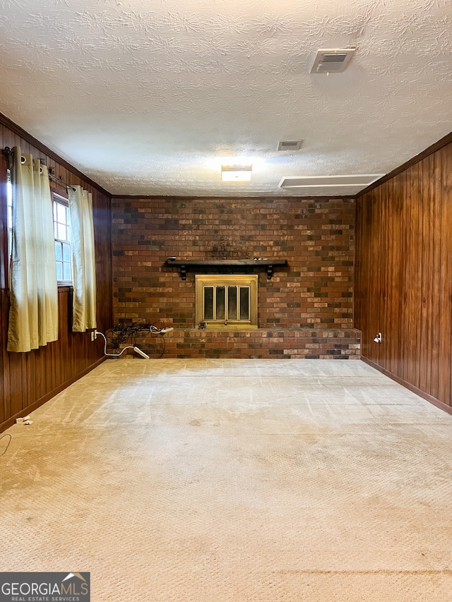 unfurnished living room with a textured ceiling, a brick fireplace, light carpet, wooden walls, and ornamental molding