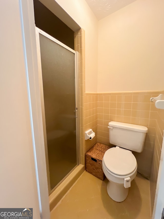 bathroom featuring a shower with door, tile walls, and toilet