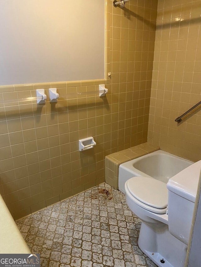 bathroom with toilet, tiled shower / bath combo, and tile walls