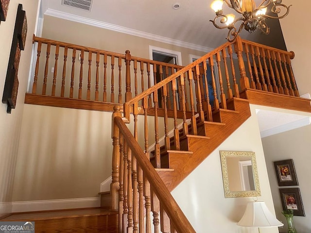 stairway with ornamental molding, an inviting chandelier, and hardwood / wood-style floors