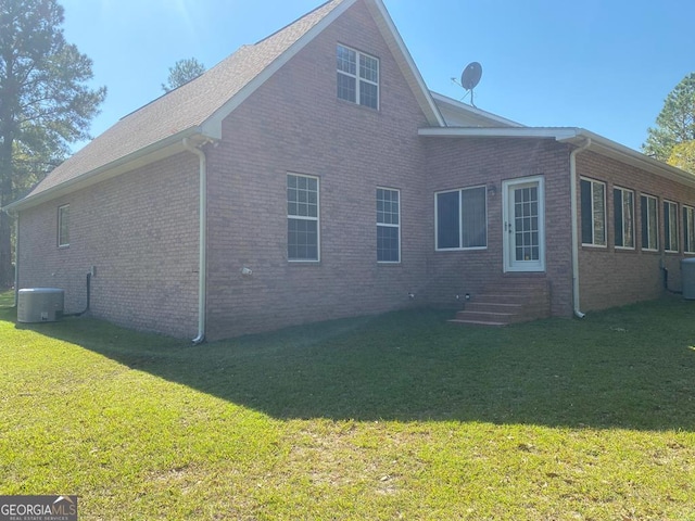 rear view of property with central air condition unit and a lawn