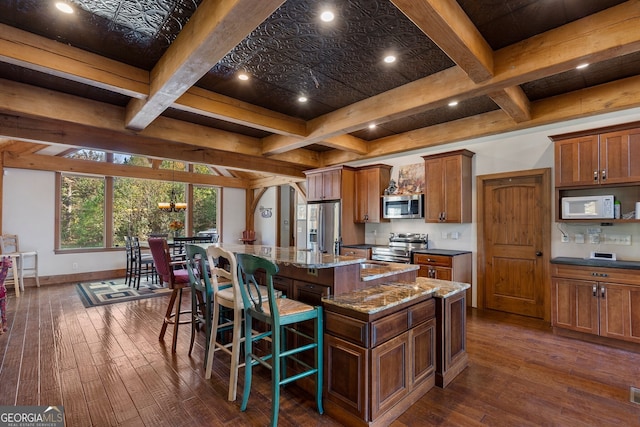 kitchen with a spacious island, appliances with stainless steel finishes, a kitchen bar, dark hardwood / wood-style floors, and beamed ceiling