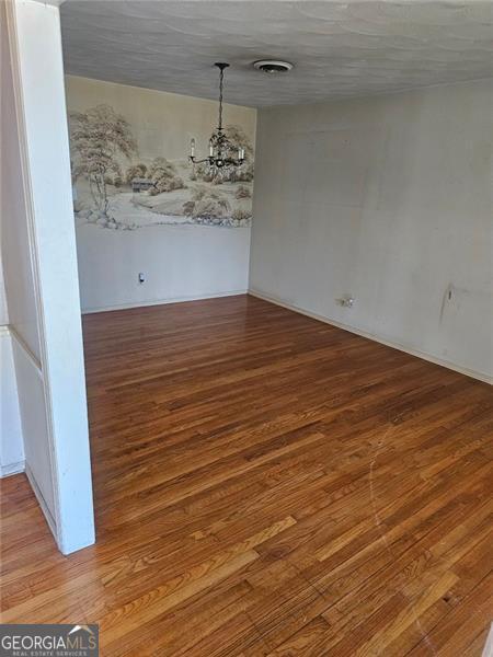 unfurnished dining area featuring hardwood / wood-style flooring, a textured ceiling, and a chandelier