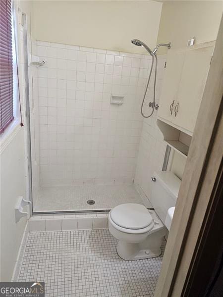 bathroom with tile patterned floors, a tile shower, and toilet