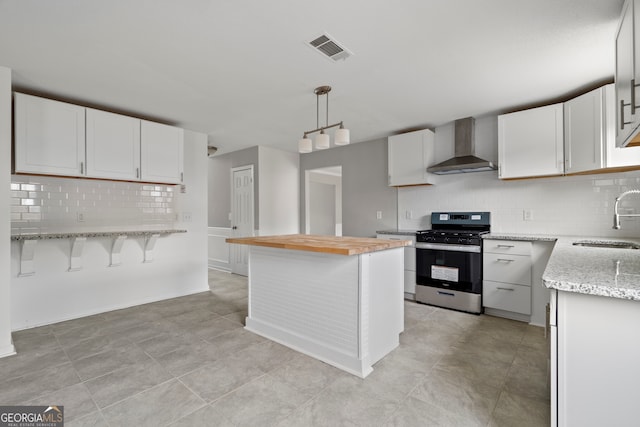 kitchen featuring white cabinetry, pendant lighting, stainless steel range, wall chimney exhaust hood, and sink