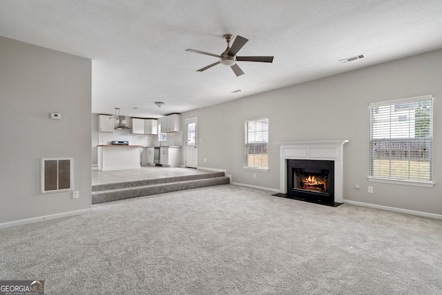 unfurnished living room with light colored carpet, a healthy amount of sunlight, and ceiling fan