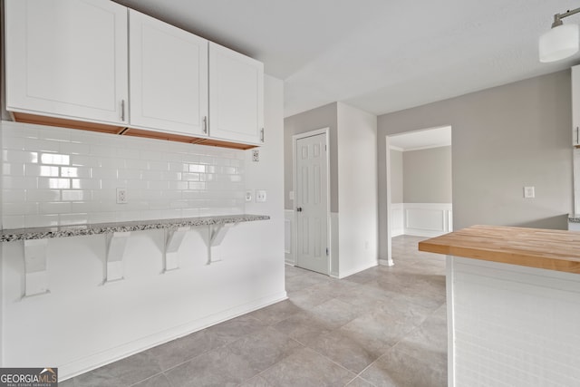 kitchen featuring white cabinetry, light stone countertops, light tile patterned flooring, and tasteful backsplash