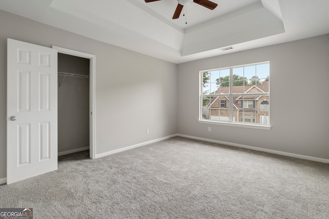 unfurnished bedroom featuring a closet, carpet flooring, a raised ceiling, and ceiling fan