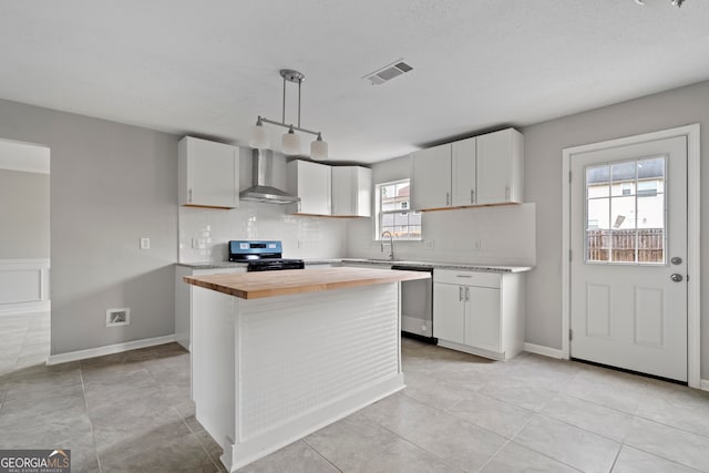 kitchen featuring wall chimney range hood, black gas stove, hanging light fixtures, stainless steel dishwasher, and white cabinetry