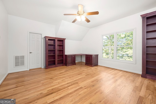 unfurnished office with built in desk, ceiling fan, vaulted ceiling, and light wood-type flooring