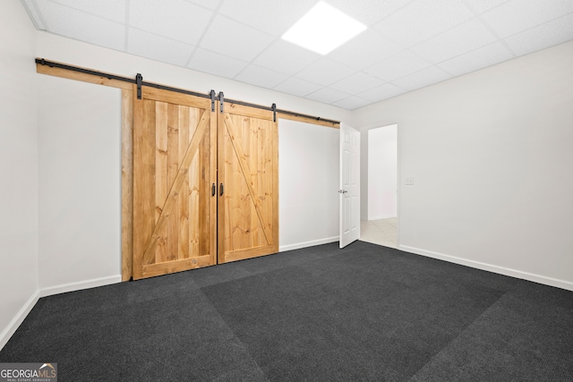 unfurnished bedroom with a drop ceiling, a barn door, and dark colored carpet