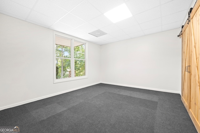 unfurnished room with a paneled ceiling, a barn door, and carpet