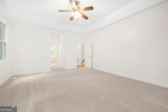 empty room with ceiling fan, ornamental molding, a tray ceiling, and light colored carpet