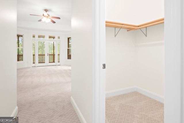 walk in closet with light carpet, french doors, and ceiling fan