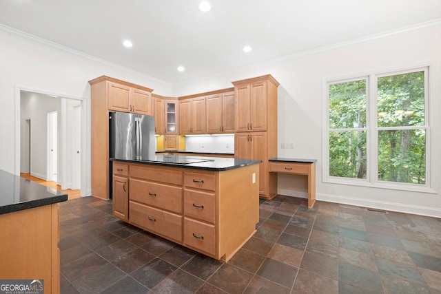 kitchen featuring cooktop, light brown cabinetry, a kitchen island, ornamental molding, and stainless steel refrigerator